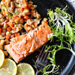 Salmon fillets cooked in a cast iron skillet with Spring vegetable ragout, frizee lettuce and lemon slices