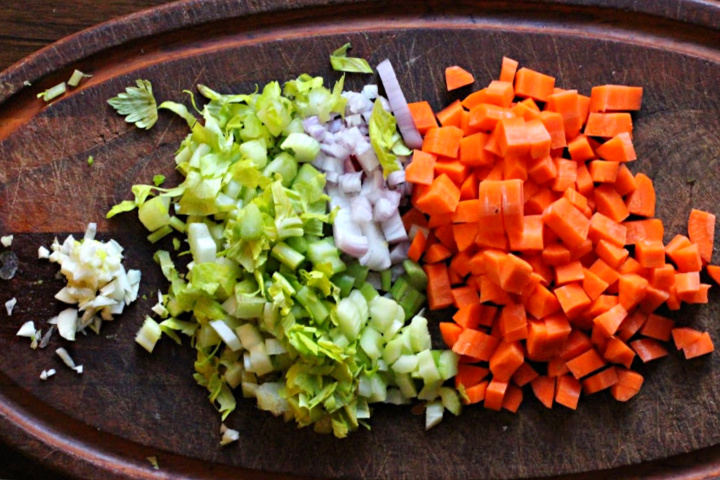 Chopped carrots, shallots, celery and garlic on a wood cutting board