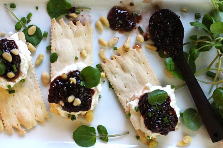 Wafer crackers topped with whipped chevre cheese and Heidi's red chile raspberry jam. On a white platter garnished with pinyon nuts and watercress