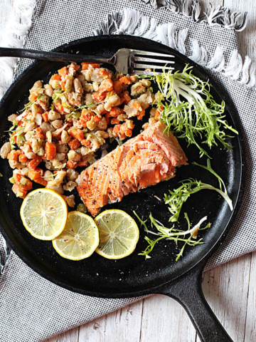 Coho salmon on a cast iron skillet with mixed vegetables ragout and lemon slices