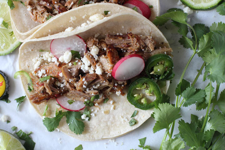 Instant Pot carnitas recipe. Pork tacos on a soft white corn taco shell garnished with sliced radishes, cotija cheese, and cilantro