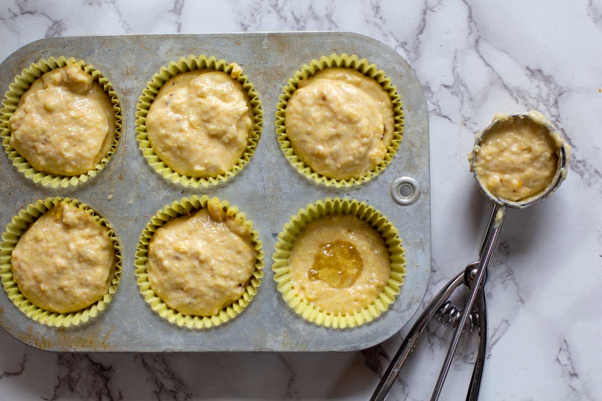 Adding jalapeno jelly to half filled corn muffins in a muffin tin.