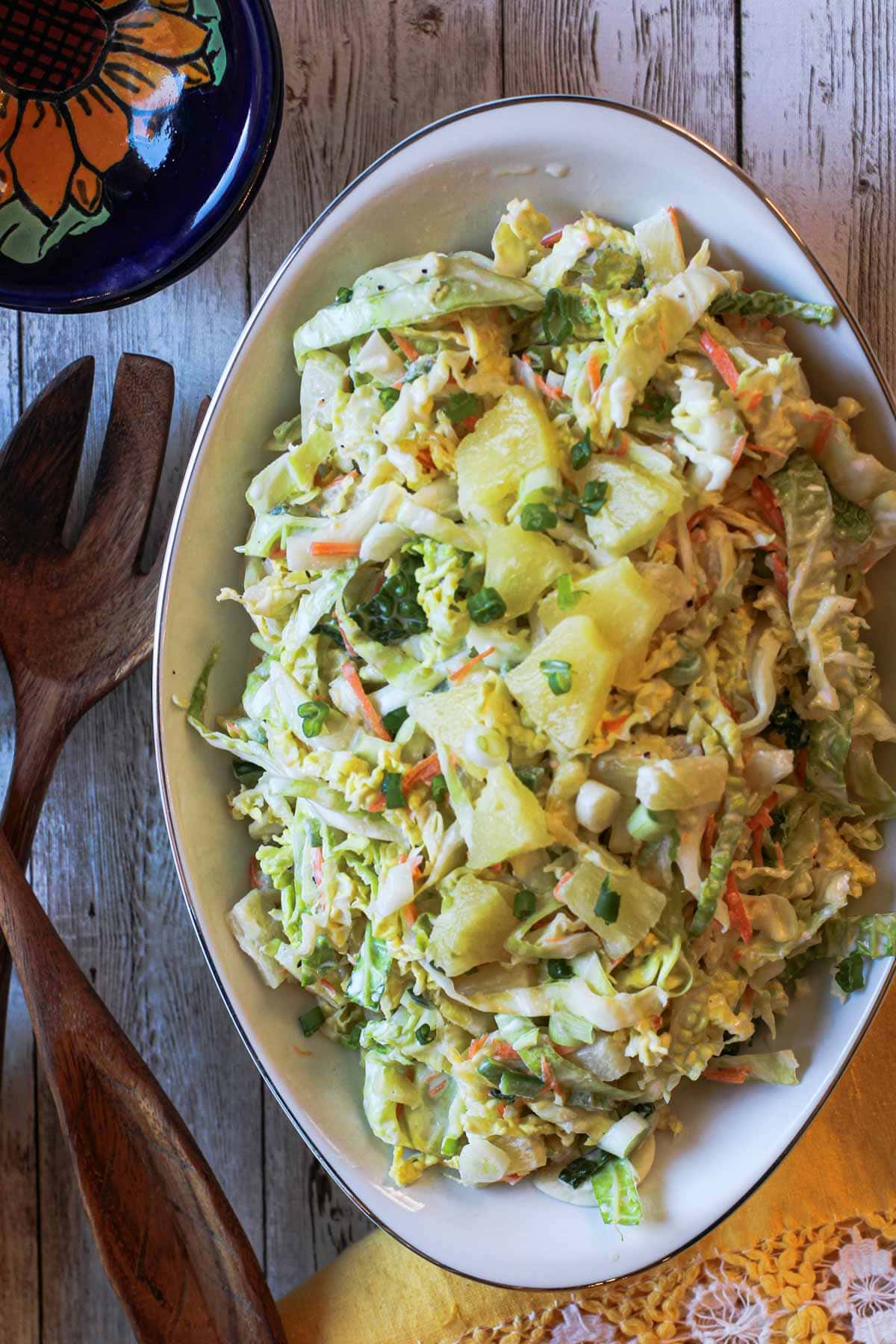 Cole Slaw with pineapple served in a white serving bowl with wooden serving tongs
