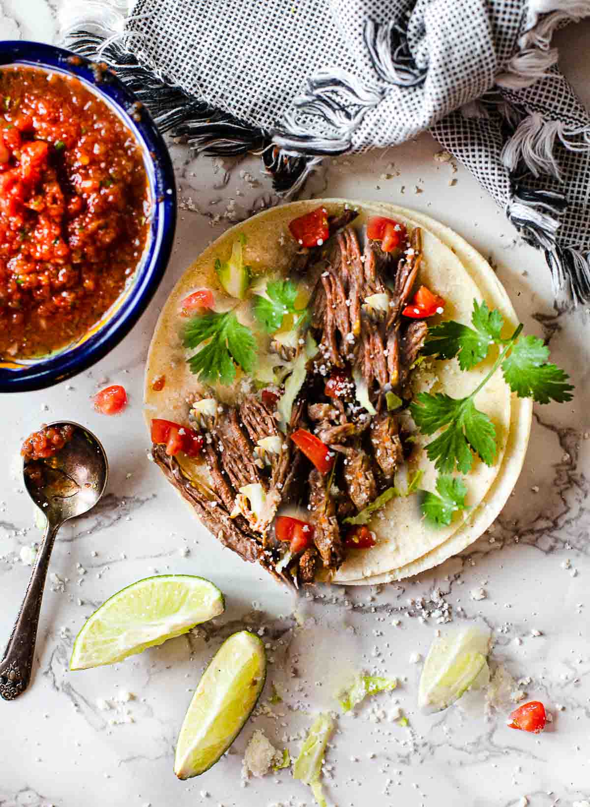 Crock Pot shredded beef tacos served with salsa and slices of lime.