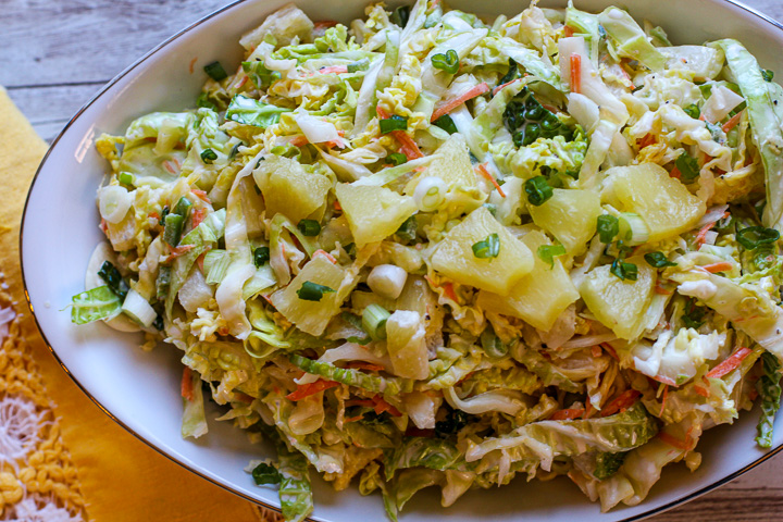 Pineapple coleslaw served in an oval white bowl. Topped with pineapple tidbits and chives.