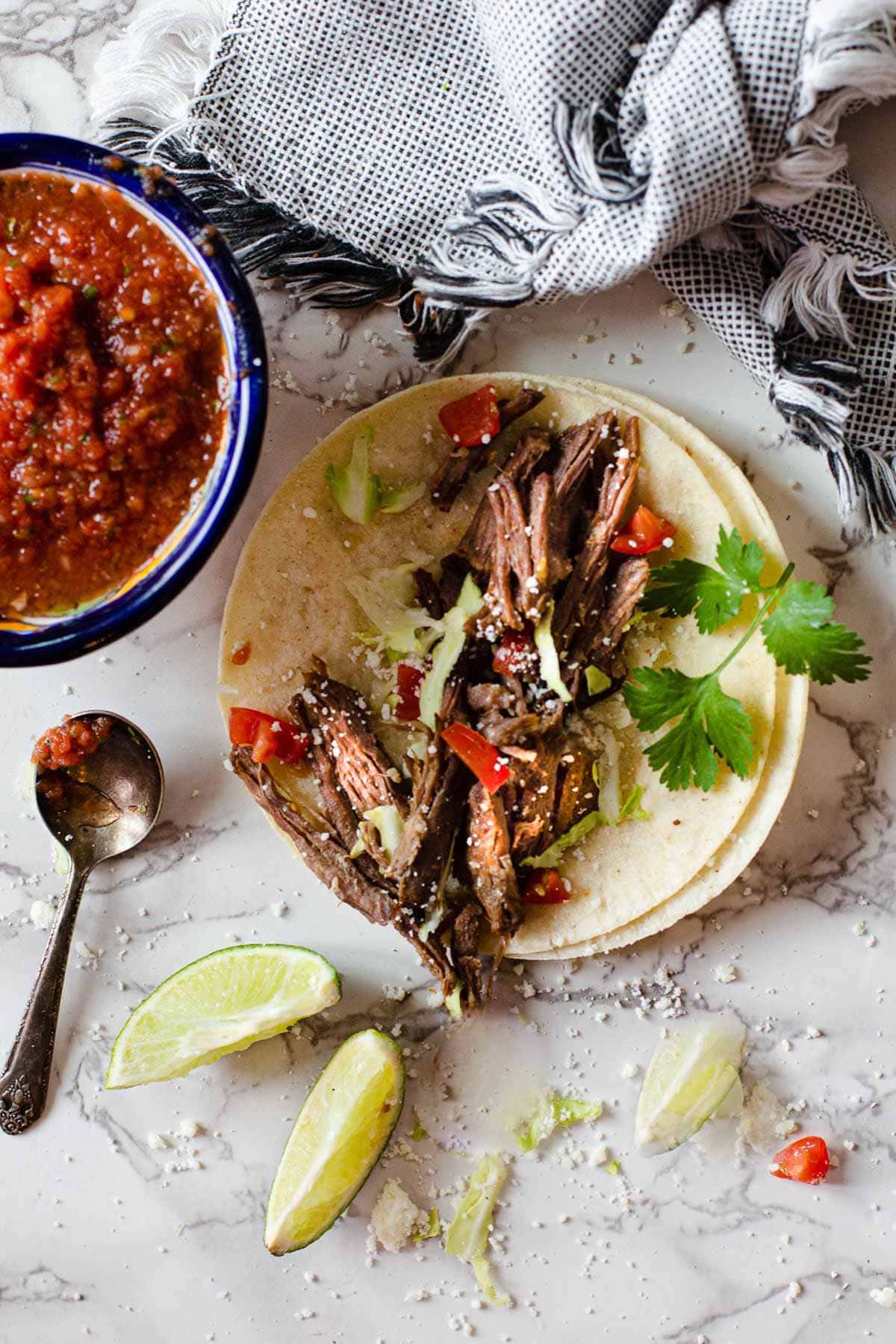 Chuck roast tacos with salsa, limes and cabbage cooked in the slow cooker