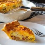 A slice of hatch green chile bacon quiche with a deep dish pie pan with quiche and spatula