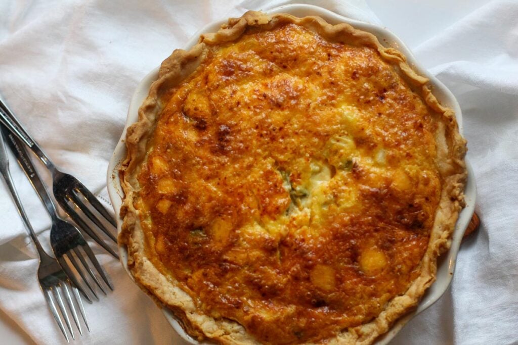 Hatch chile and bacon quiche on white linens with forks