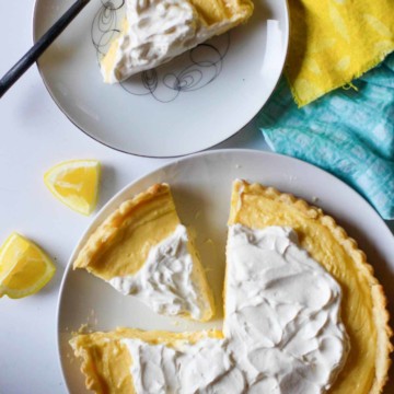 A lemon tart on a white plate with a slice of lemon tart next to it.