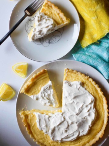 A lemon tart on a white plate with a slice of lemon tart next to it.