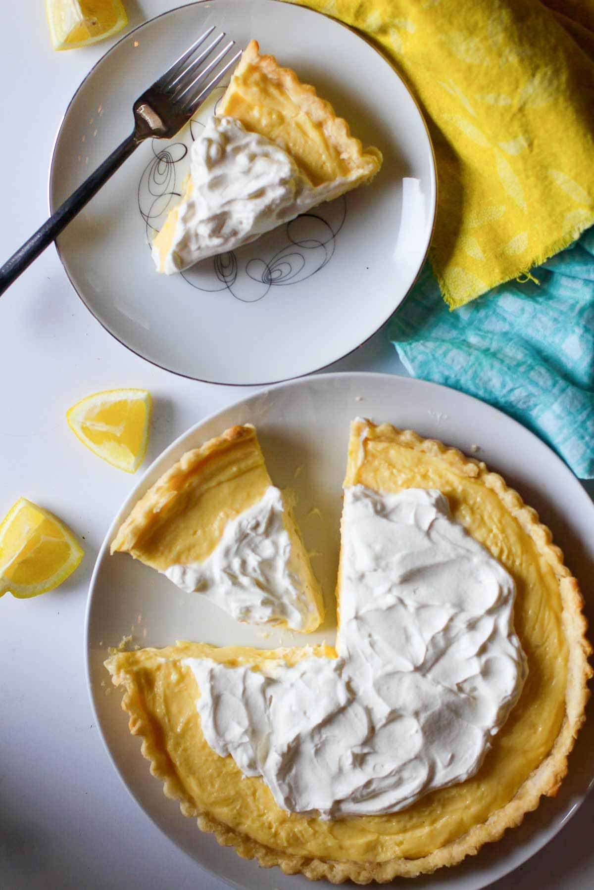 A lemon tart on a white plate with a slice of lemon tart next to it.