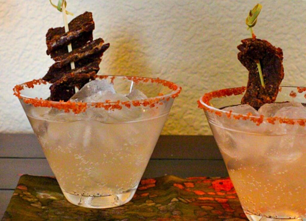 Two cocktail glasses holding salty dog cocktails with beef jerky for garnish.