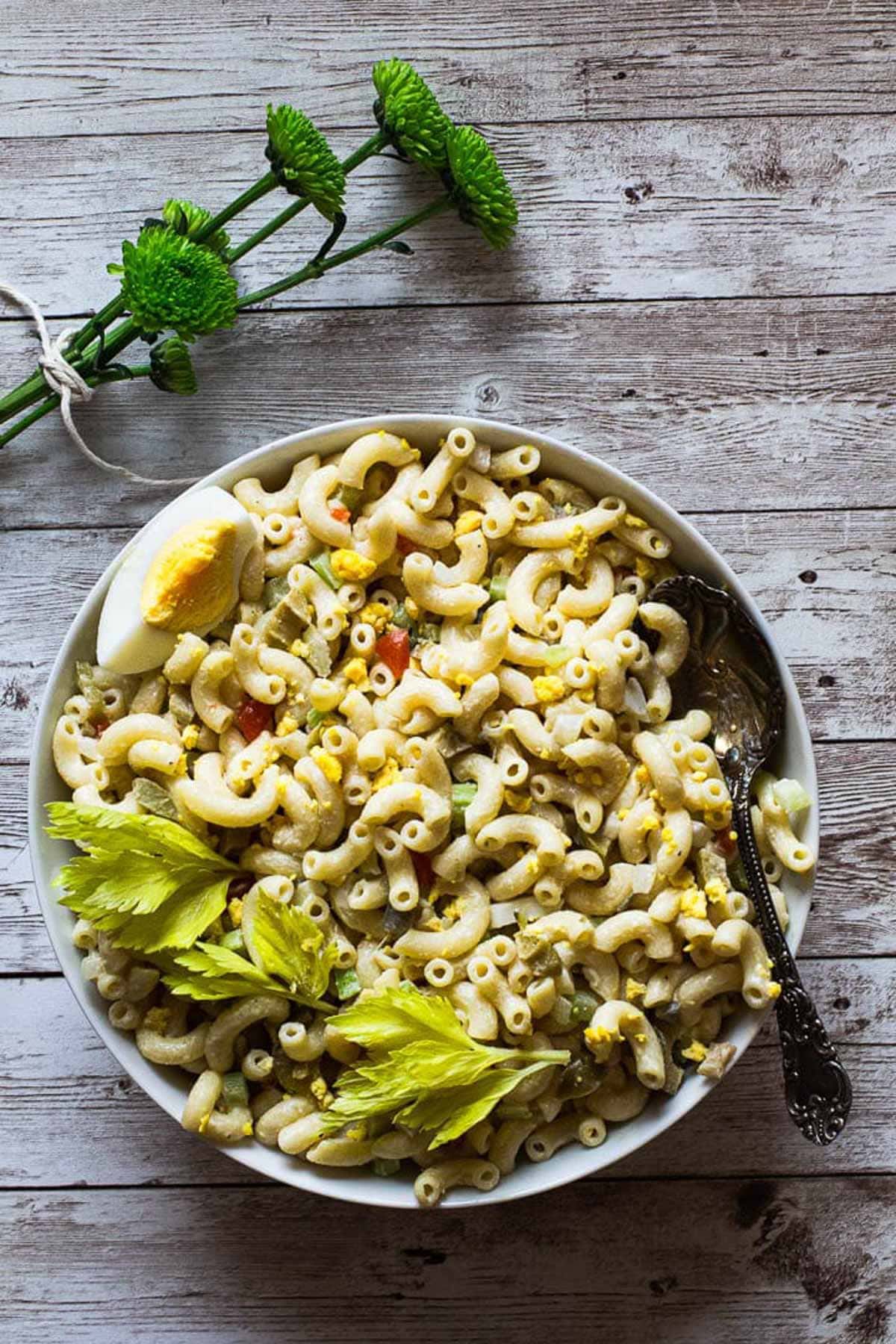 Classic old fashioned macaroni salad with elbow macaroni served in a white bowl garnished with celery leaves