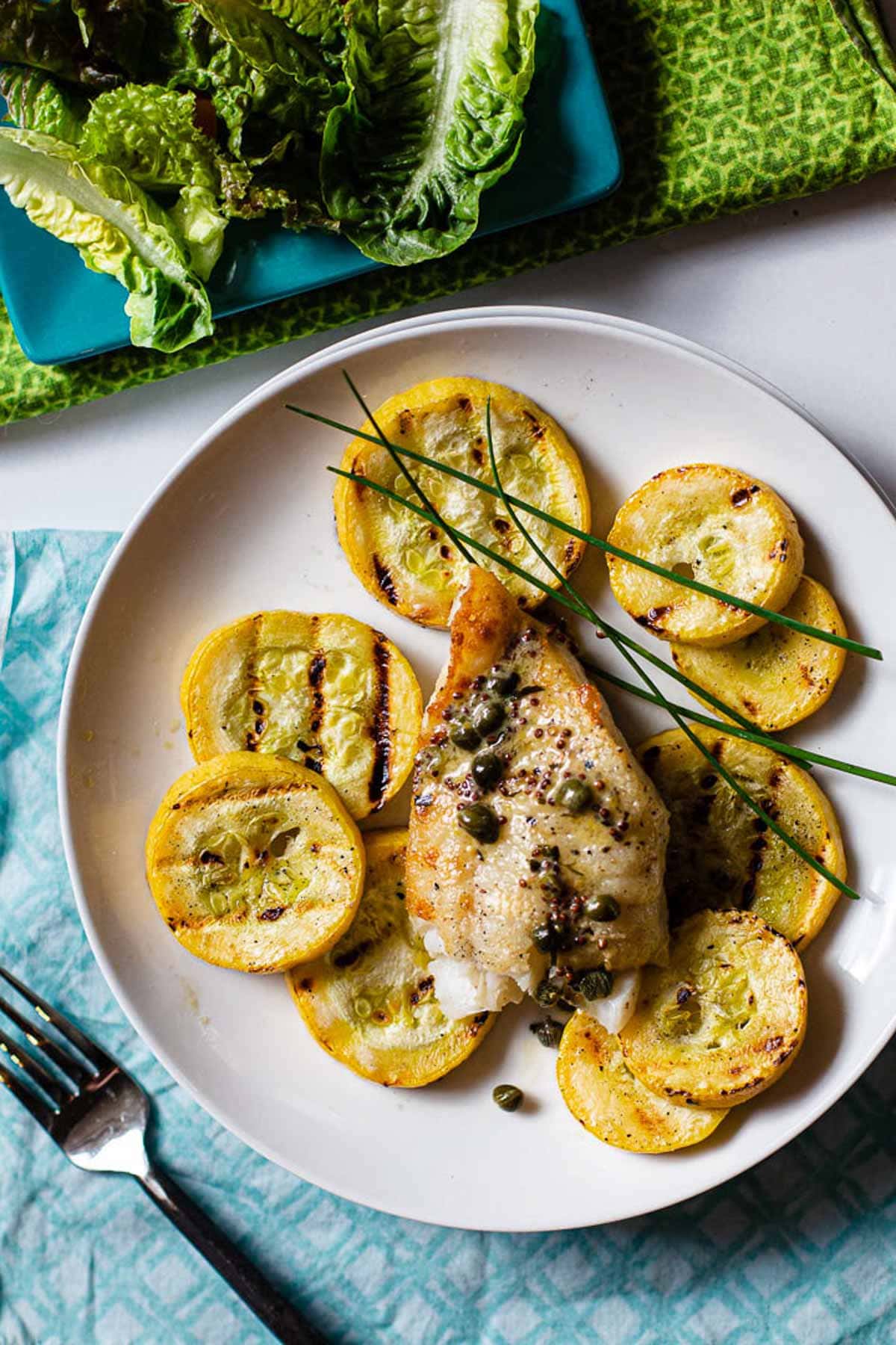 Pan fried cod served over grilled summer squash, garnished with chives and served with a side salad