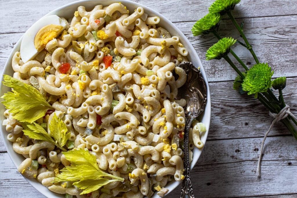 Classic macaroni salad with mayonnaise, celery, onion and green olives garnished with celery leaves and hard boiled egg