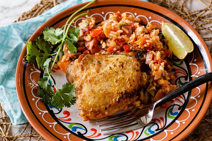 Fried chicken thigh served along siMexican rice and garnished with cilantro and lime wedge.
