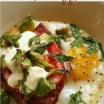 baked eggs with ham topped with fresh tomatoes, avocado and sour cream garnished with chopped cilantro