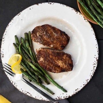 Cocoa chile powder rubbed grilled pork chops with sauteed green beans on a rustic white plate with a wedge of lemon