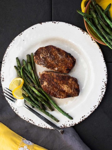 Cocoa chile powder rubbed grilled pork chops with sauteed green beans on a rustic white plate with a wedge of lemon