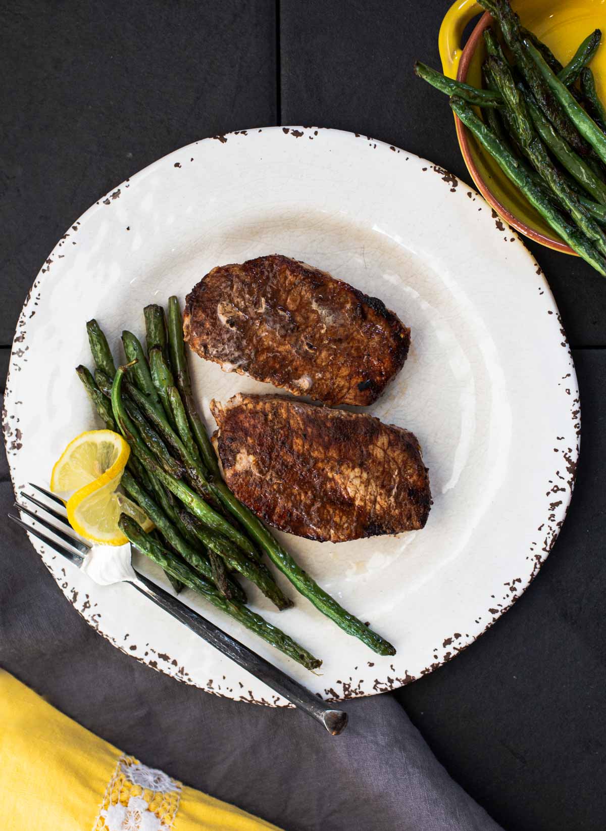 Cocoa chile powder rubbed grilled pork chops with sauteed green beans on a rustic white plate with a wedge of lemon