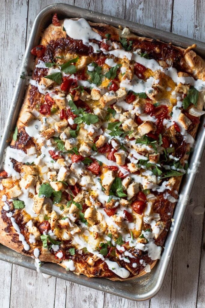 BBQ chicken pizza cooked in a sheet pan with tomatoes, jalapeno, cilantro and drizzled with ranch dressing