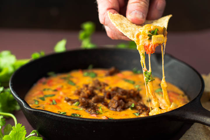 A tortilla chip dipped in queso fundido with tequila.