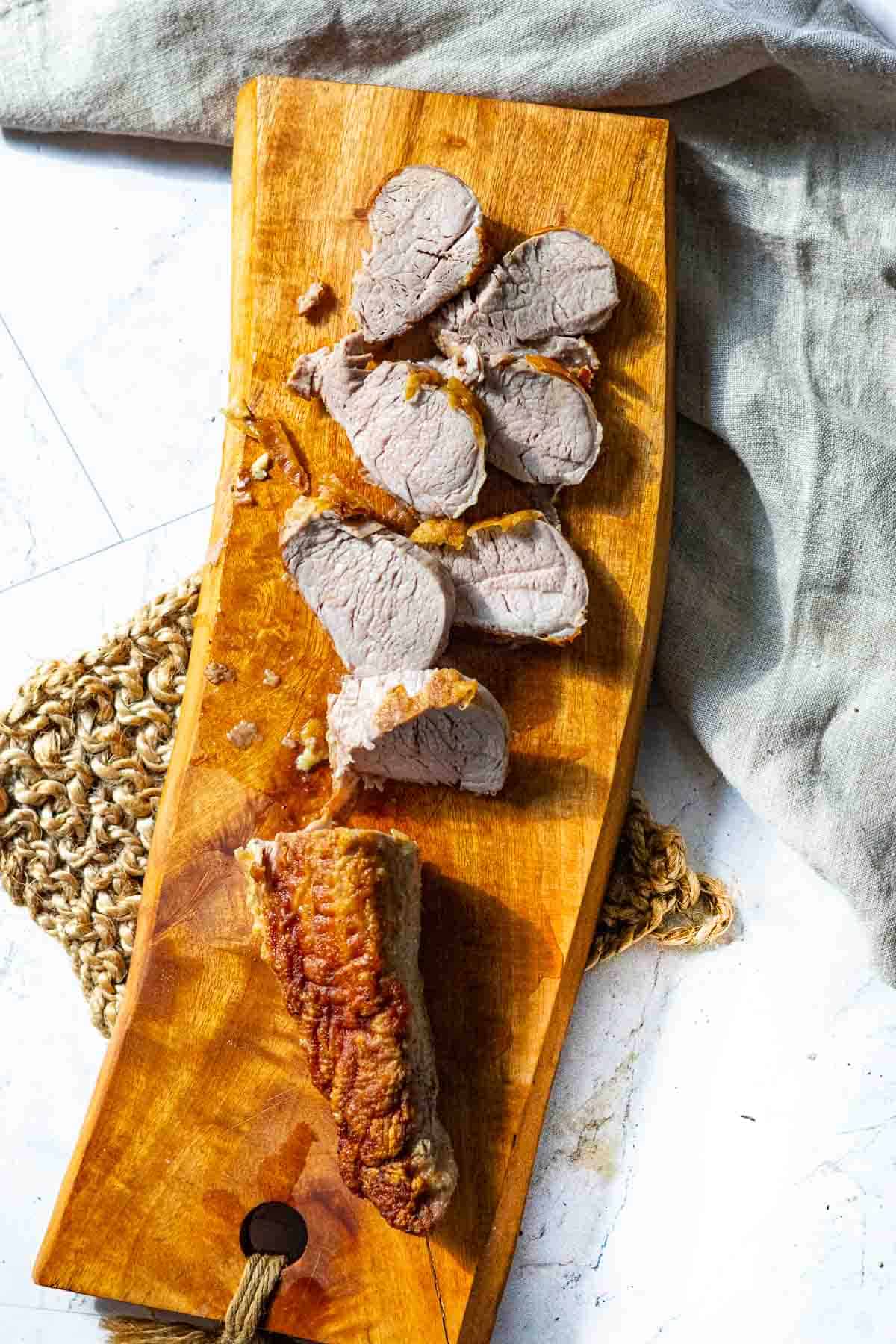 Slicing pork tenderloin into medallions on a cutting board.
