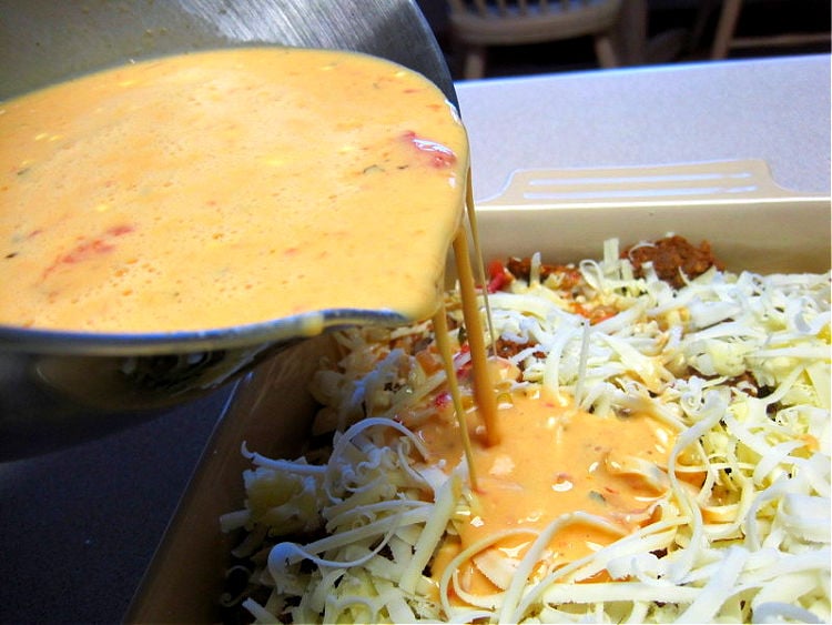 Pouring egg, salsa, sour cream custard over Mexican Breakfast Casserole