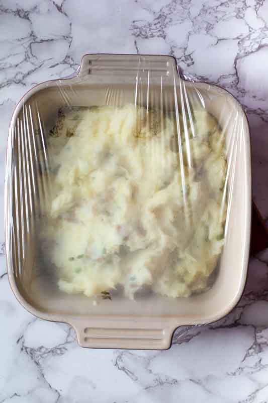 Covering sour cream mashed potatoes with plastic wrap.