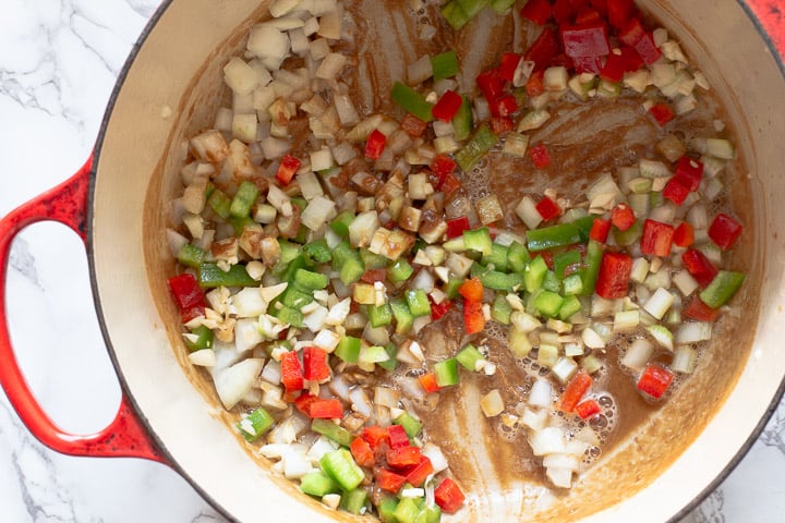 Stirring chopped vegetables into a roux to make shrimp and sausage gumbo