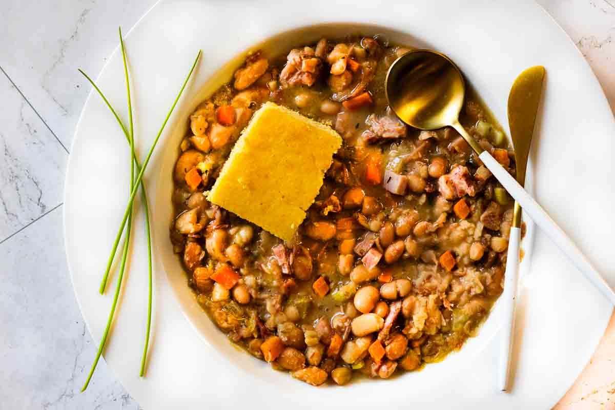 Crock pot ham and beans served in a white bowl with cornbread.