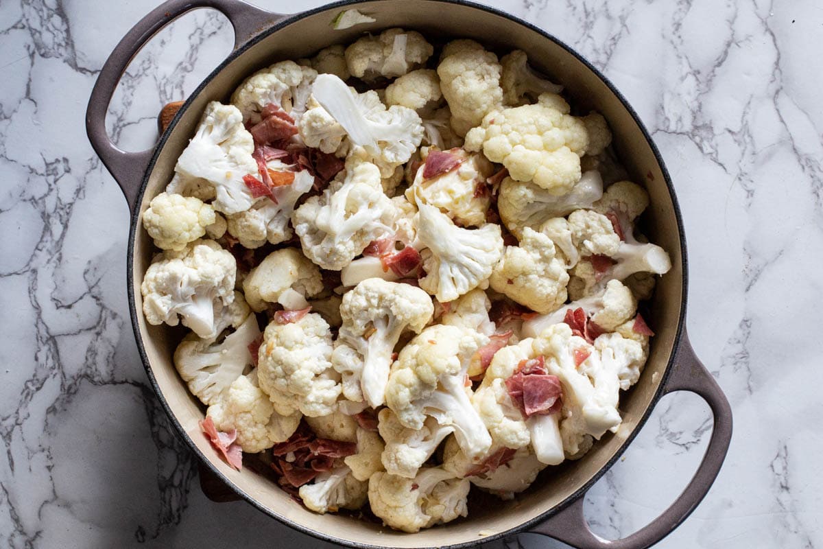 adding cauliflower to prosciutto in a dutch oven to make creamed cauliflower