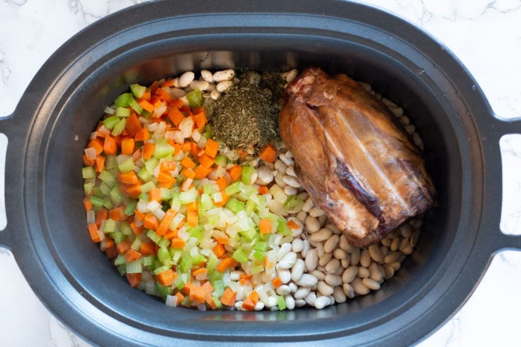 Ham hock, white beans, vegetables and seasonings in crockpot to make ham and beans