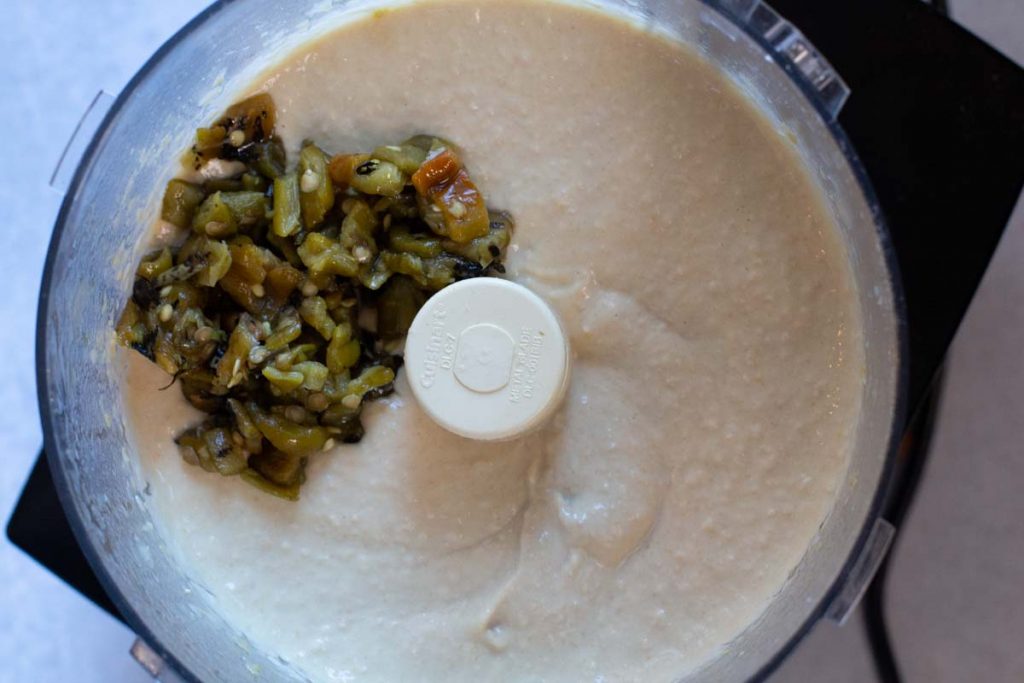 Adding green chile peppers to blended chickpeas for spicy hummus