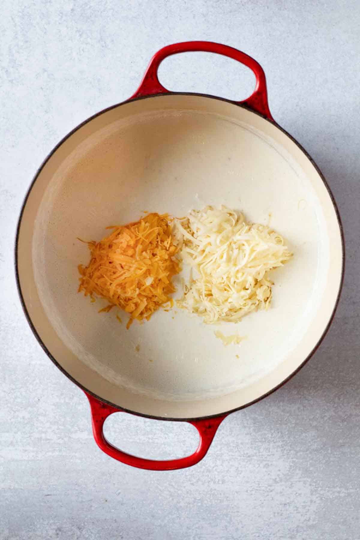 Adding cheeses to roux to make chipotle mac and cheese.