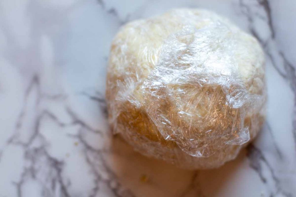 Wrapping empanada dough in plastic wrap to rest in the refrigerator.