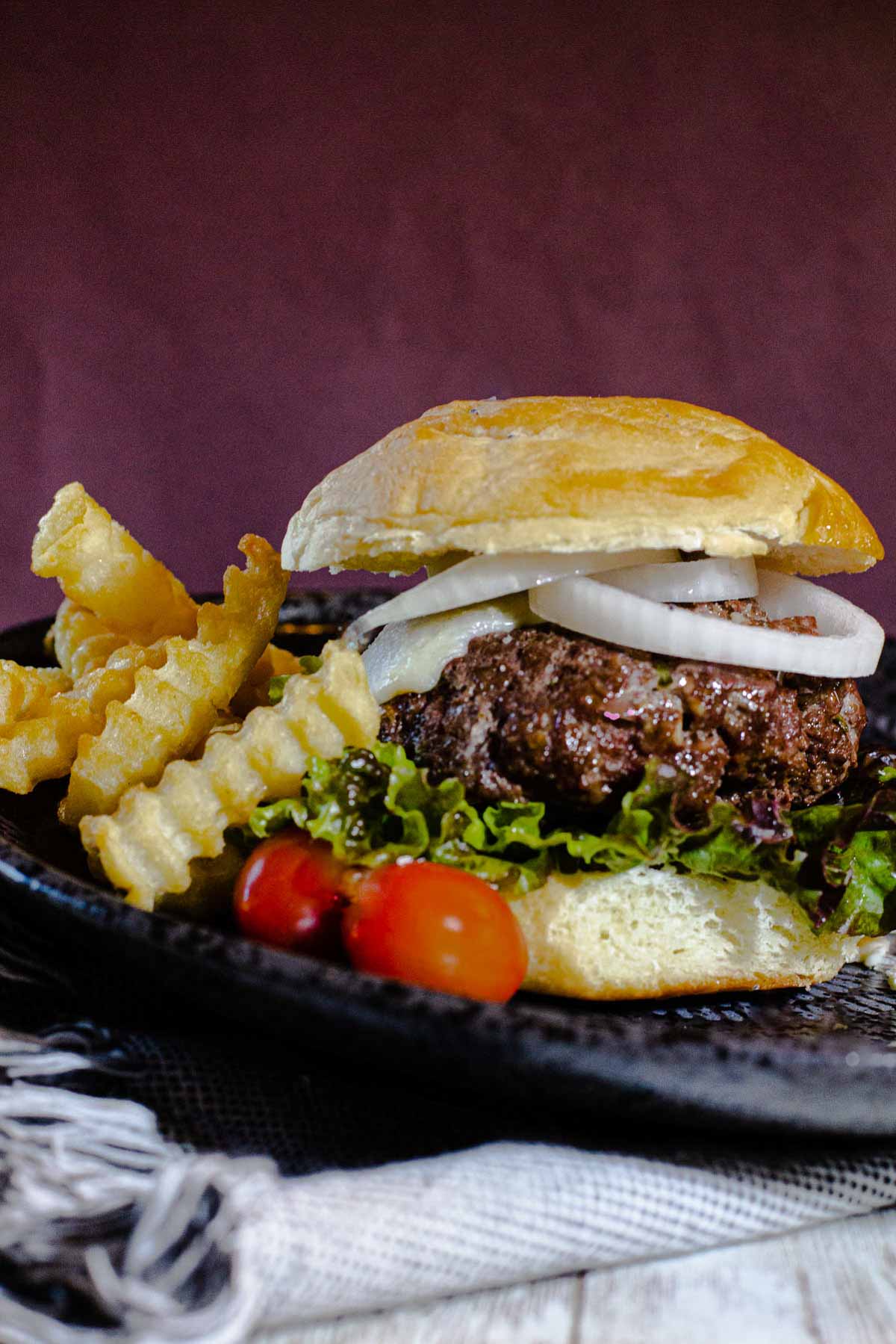 Blue cheese burger recipe topped with rings of onion and tomato with crinkle fries.