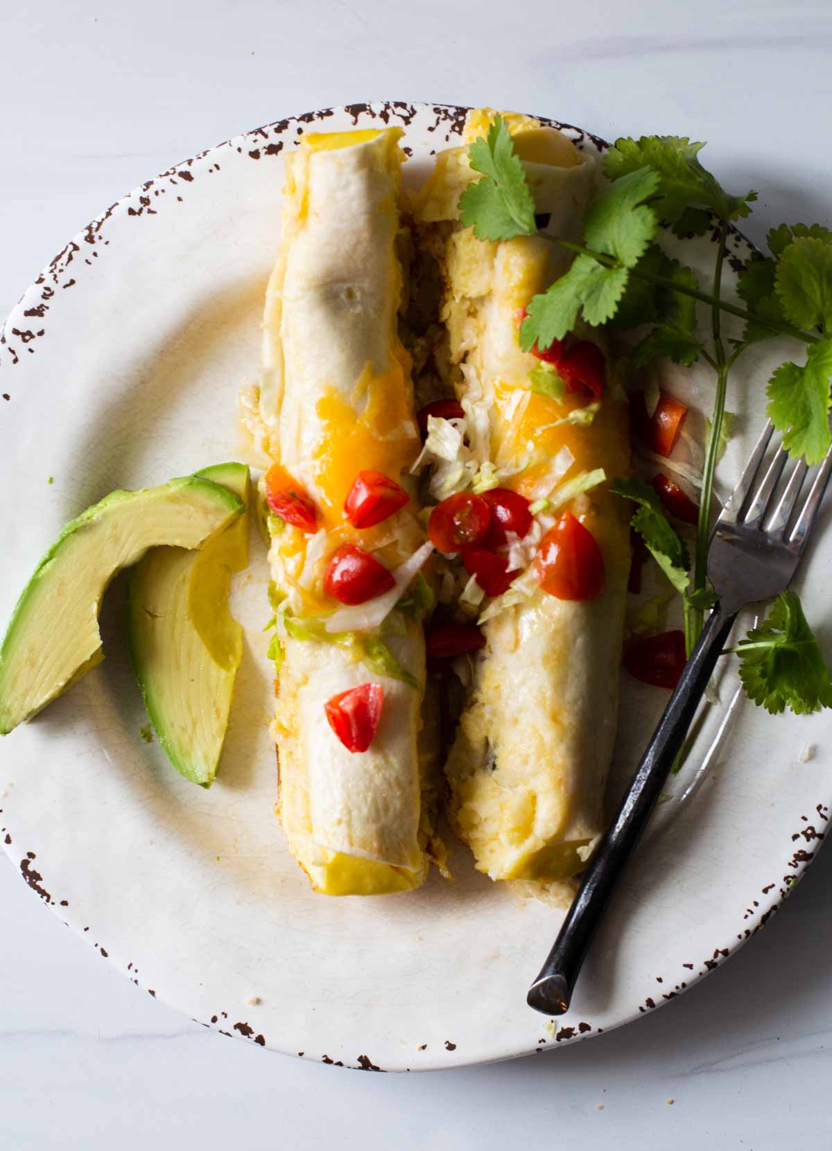two baked breakfast burritos garnished with cilantro, cherry tomatoes and avocado