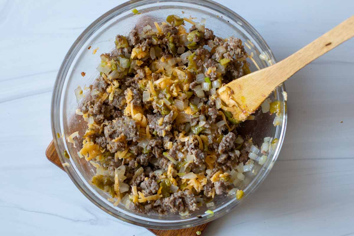 Cooked sausage, chile peppers and shredded cheese mixed together in a clear mixing bowl