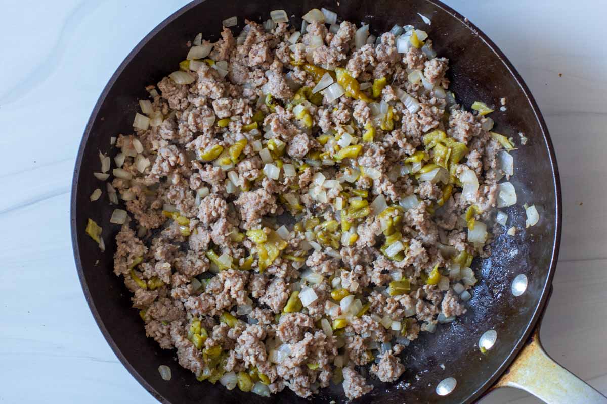 Browning sausage with onions and chile peppers in a fry pan.
