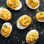 Spicy deviled eggs displayed on black platter.