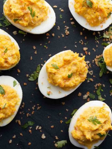 Spicy deviled eggs displayed on black platter.