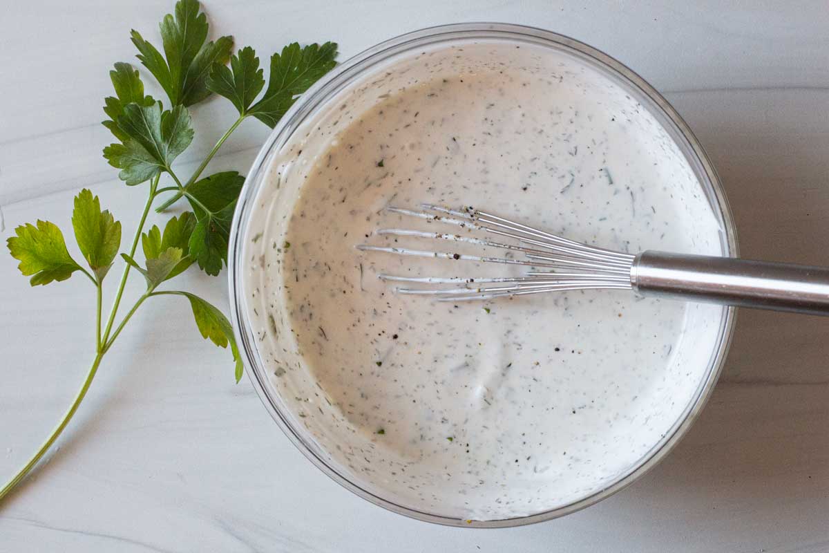 Buttermilk ranch dressing recipe made in a clear bowl using a whisk and garnished with fresh parsley