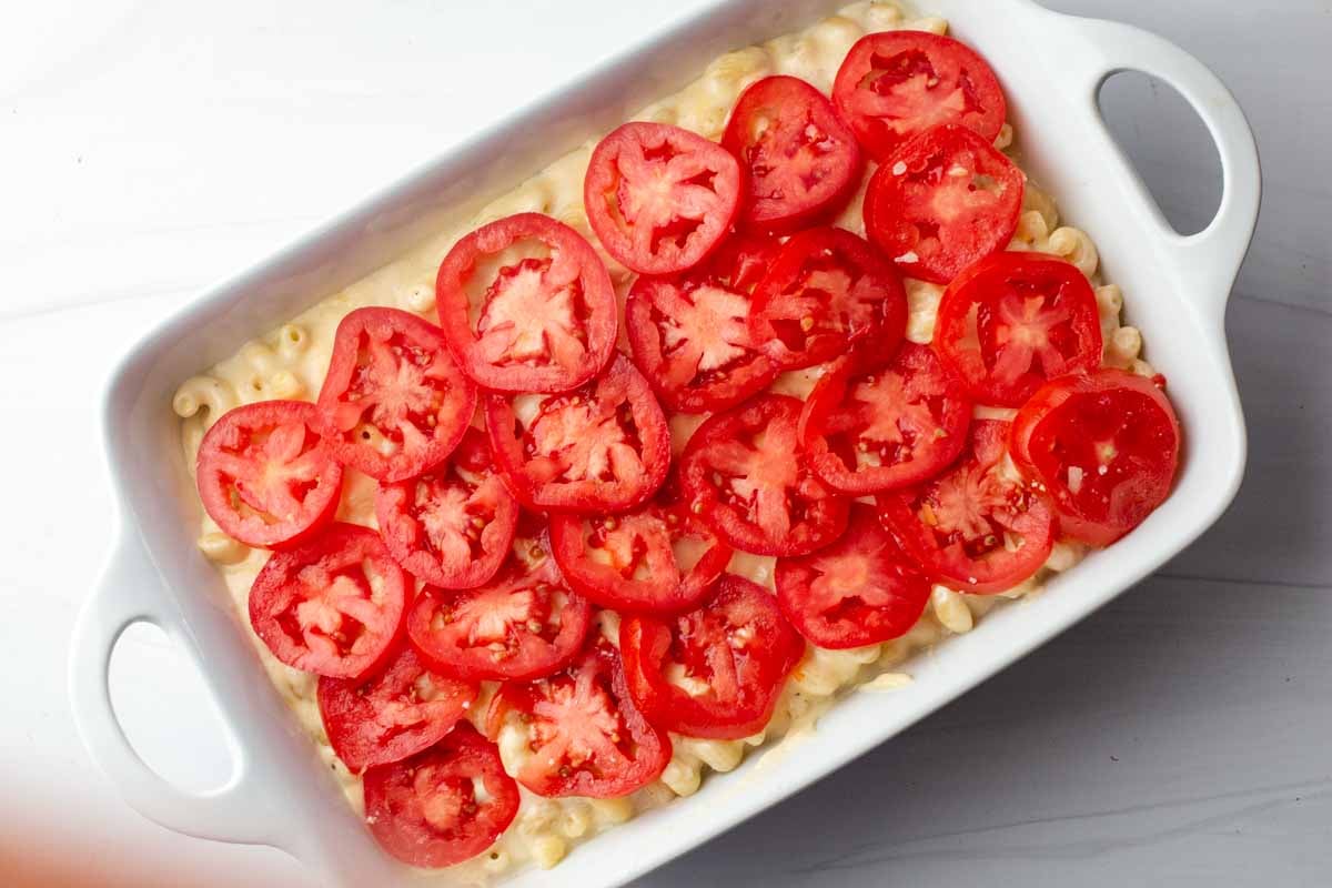 Sliced tomatoes on mac and cheese in a white casserole dish ready to bake