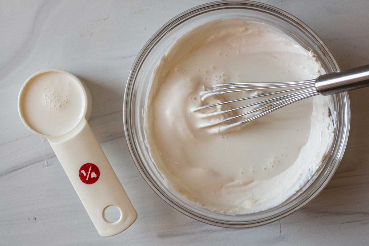 Whisking buttermilk in with mayonnaise and sour cream to make dressing