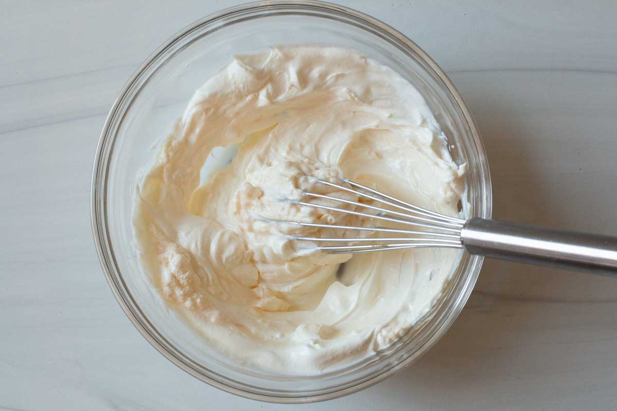 Mixing together mayo and sour cream with a whisk in a glass bowl.