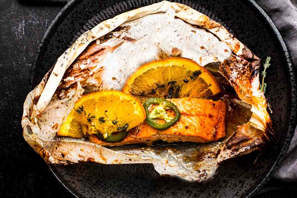 Salmon in parchment paper topped with jalapeno pepper and orange.