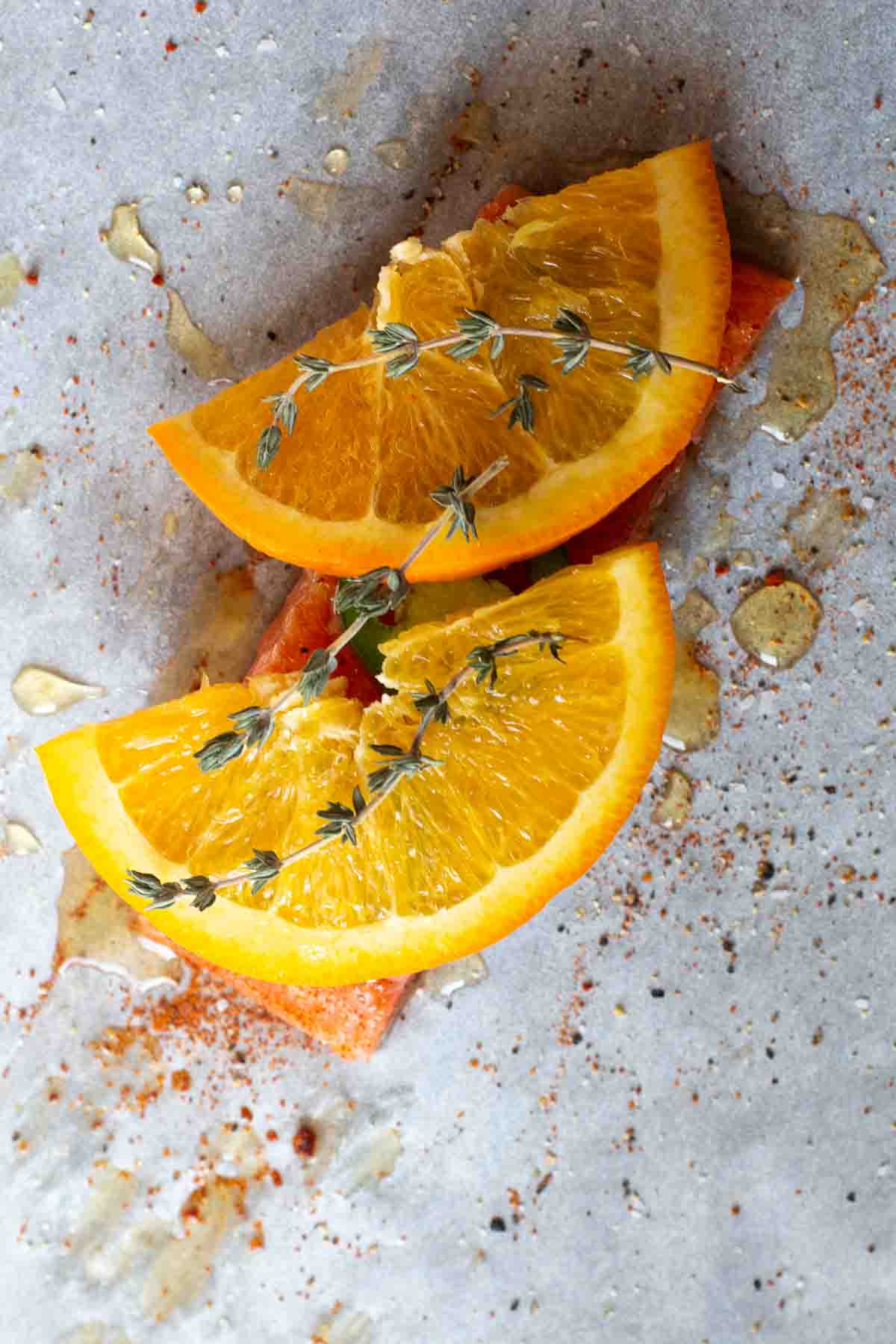 Step 4: placing orange slices and fresh thyme on salmon to make salmon in parchment paper.