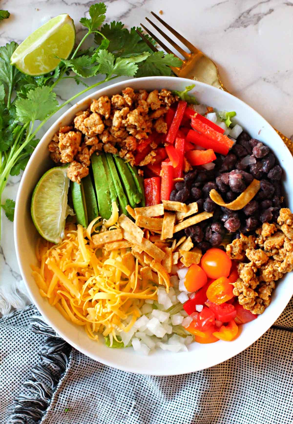 Chicken burrito bowl made with ground chicken breast served over rice and topped with cheese, black beans, avocado, red bell pepper, onions and cherry tomatoes.