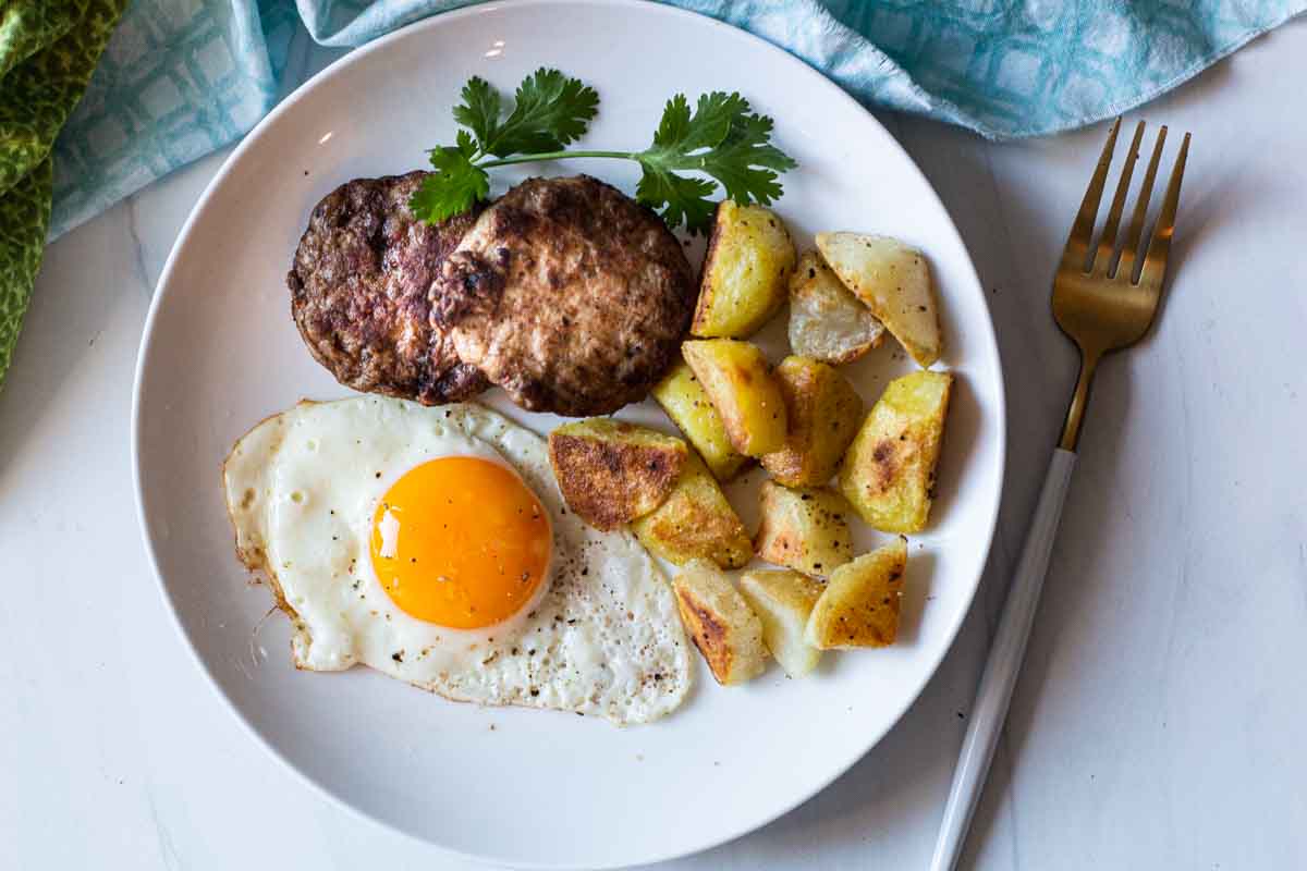 Ground turkey sausage patties with fried potatoes and a fried egg.